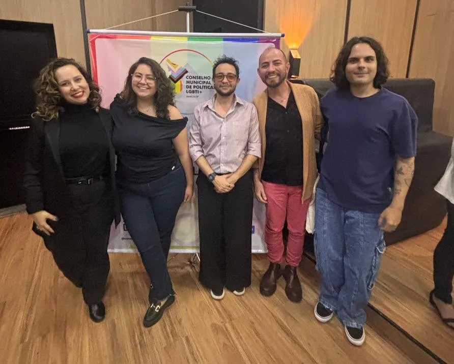 Gabriel Meyer com um grupo diante do banner do Conselho Municipal de Políticas LGBTI+ de Marília